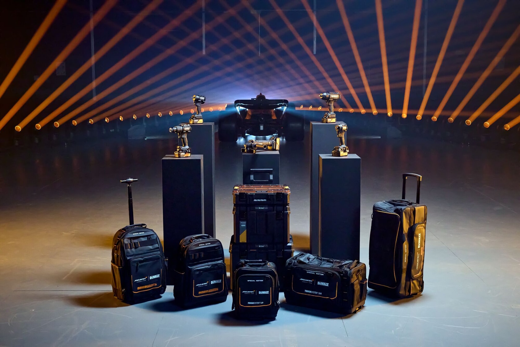 Bolsas e caixas DEWALT com furadeiras exibidas diante de um carro de corrida e iluminação marcante.